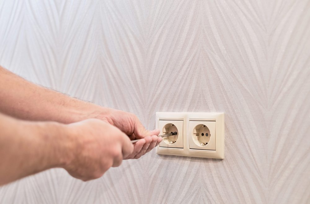 Installation of sockets in a new apartment. Close up on hands of caucasian man electrician holding screwdriver working on the plug electric on residential electric system