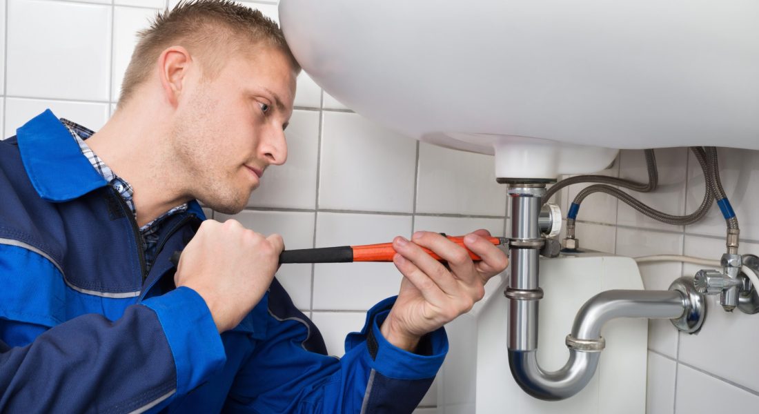 Male Plumber Fixing Sink In Bathroom